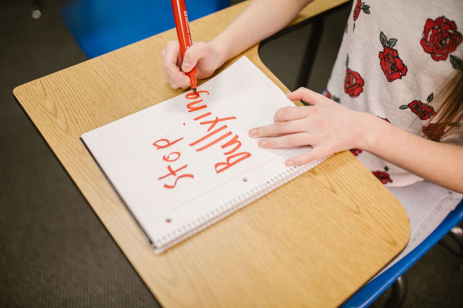 A child writes 'Stop Bullying' in a notebook on a school desk, promoting awareness.