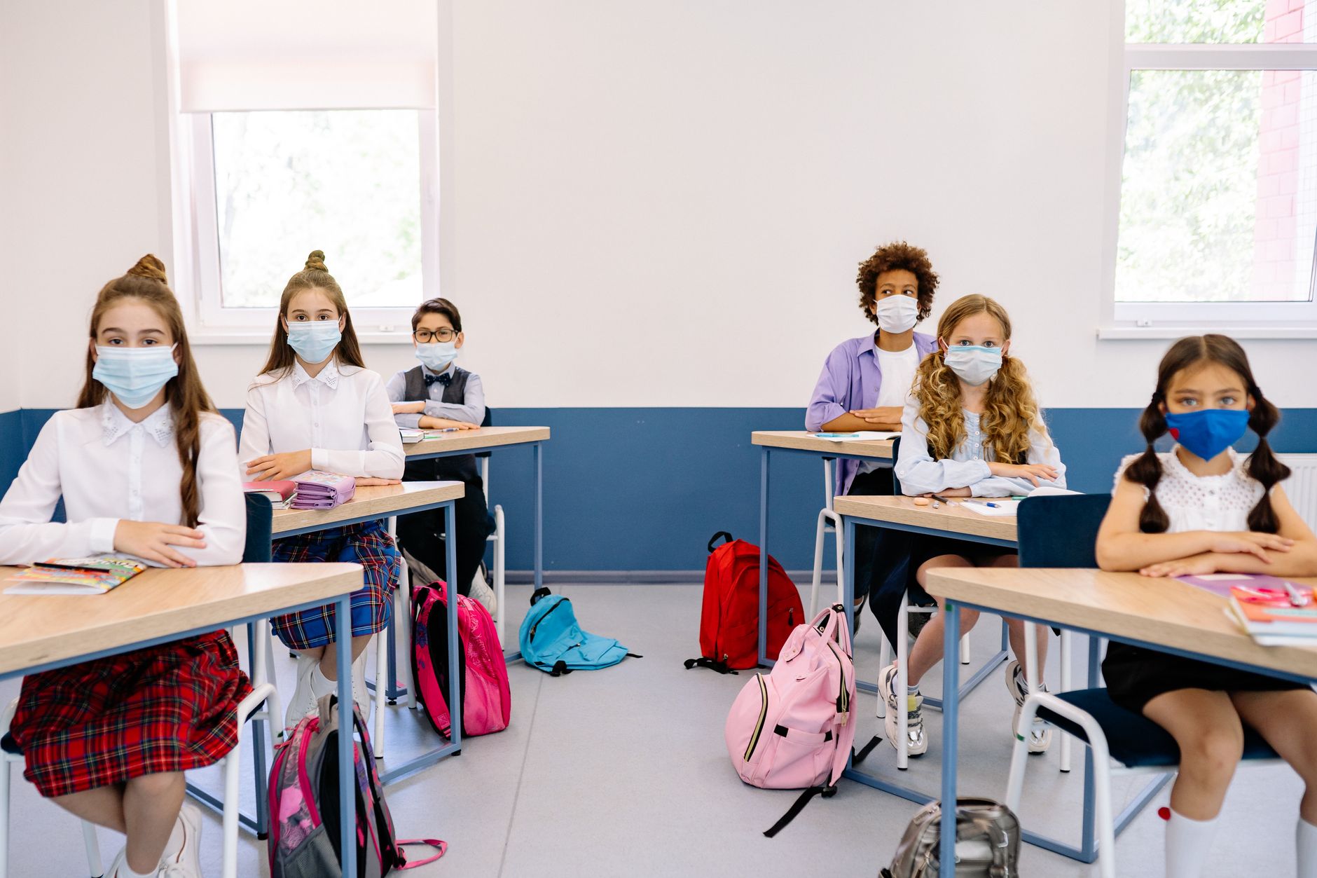 Students in masks seated at desks in a classroom, maintaining safety measures.