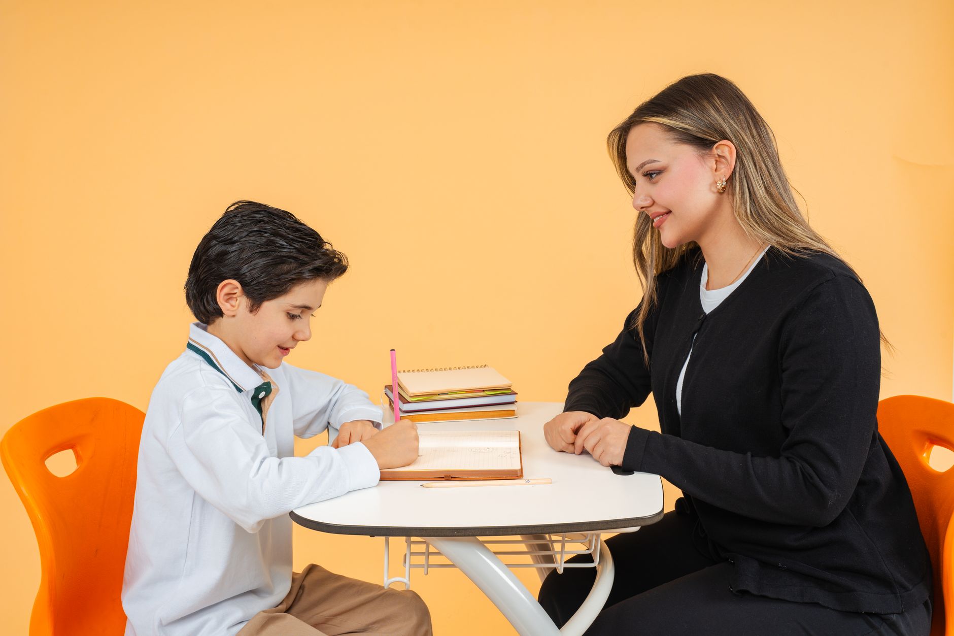 A teacher helps a student with schoolwork at a desk in a bright classroom.