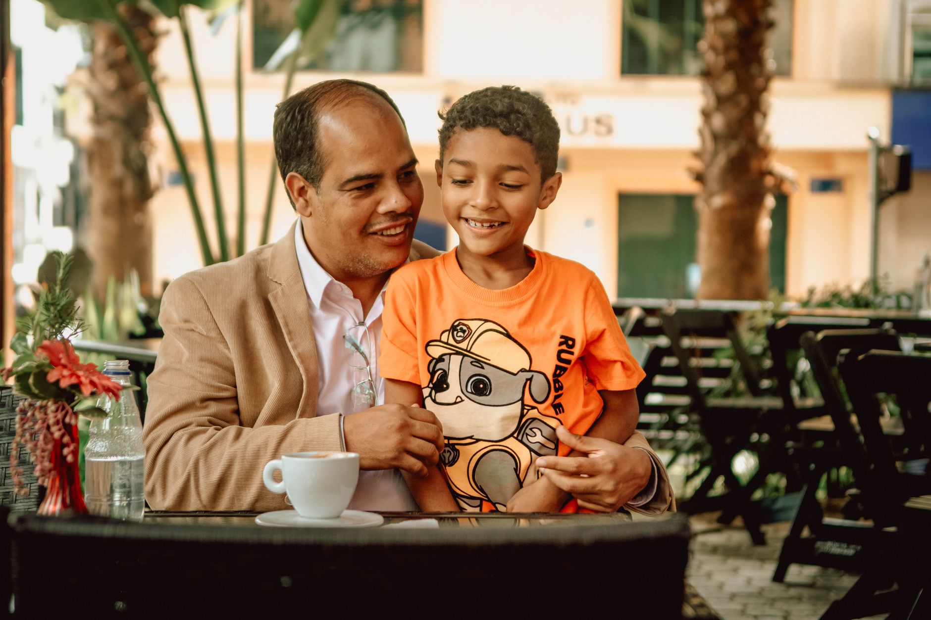 Heartwarming moment of a father and son sharing a coffee at an outdoor café, full of joy.