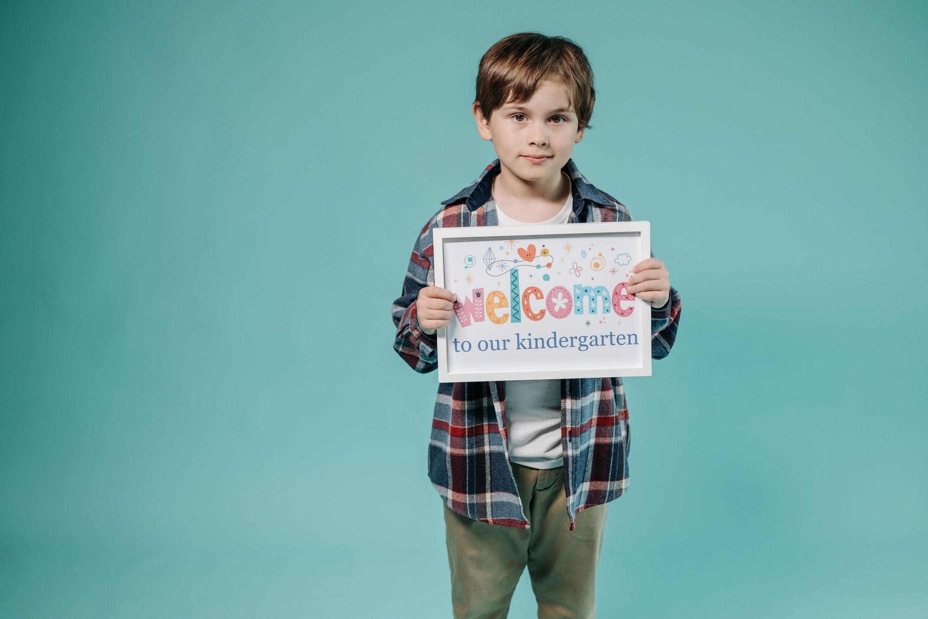 Young boy with sign welcomes viewers to kindergarten, studio photo.